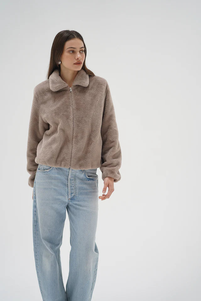 Woman wearing a brown fleece jacket and light blue jeans on a white background