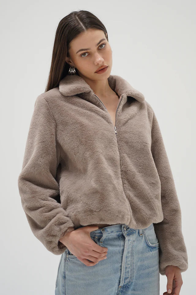 Woman wearing a brown fleece jacket and blue jeans on a white background
