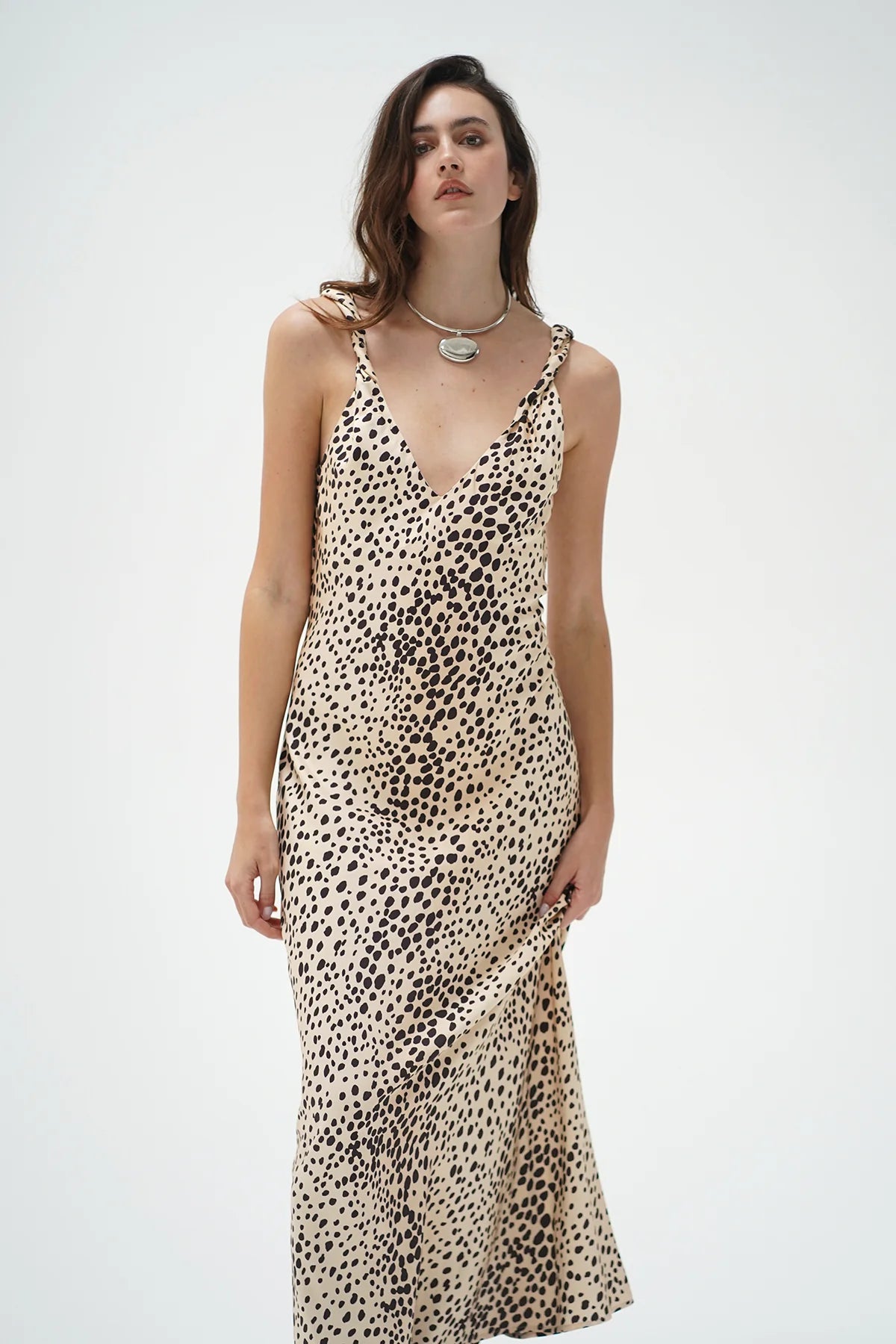 A woman modeling a sleeveless V-neck maxi dress with a beige and black leopard print pattern, set against a plain light gray studio background.