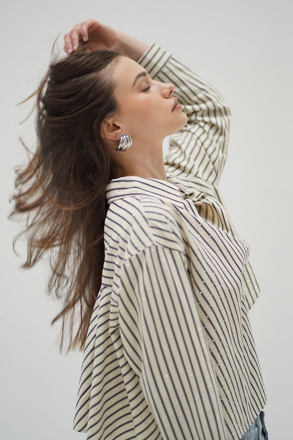 Woman wearing a striped shirt with her hair blowing in the wind against a plain background side view