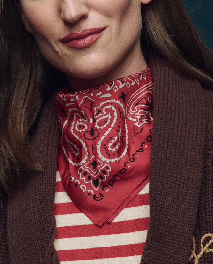 Person wearing a red bandana with white patterns over a striped shirt and brown jacket.