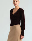 A model wearing a dark brown long-sleeve wrap-style top and a beige knit pencil skirt, photographed against a light gray studio background.