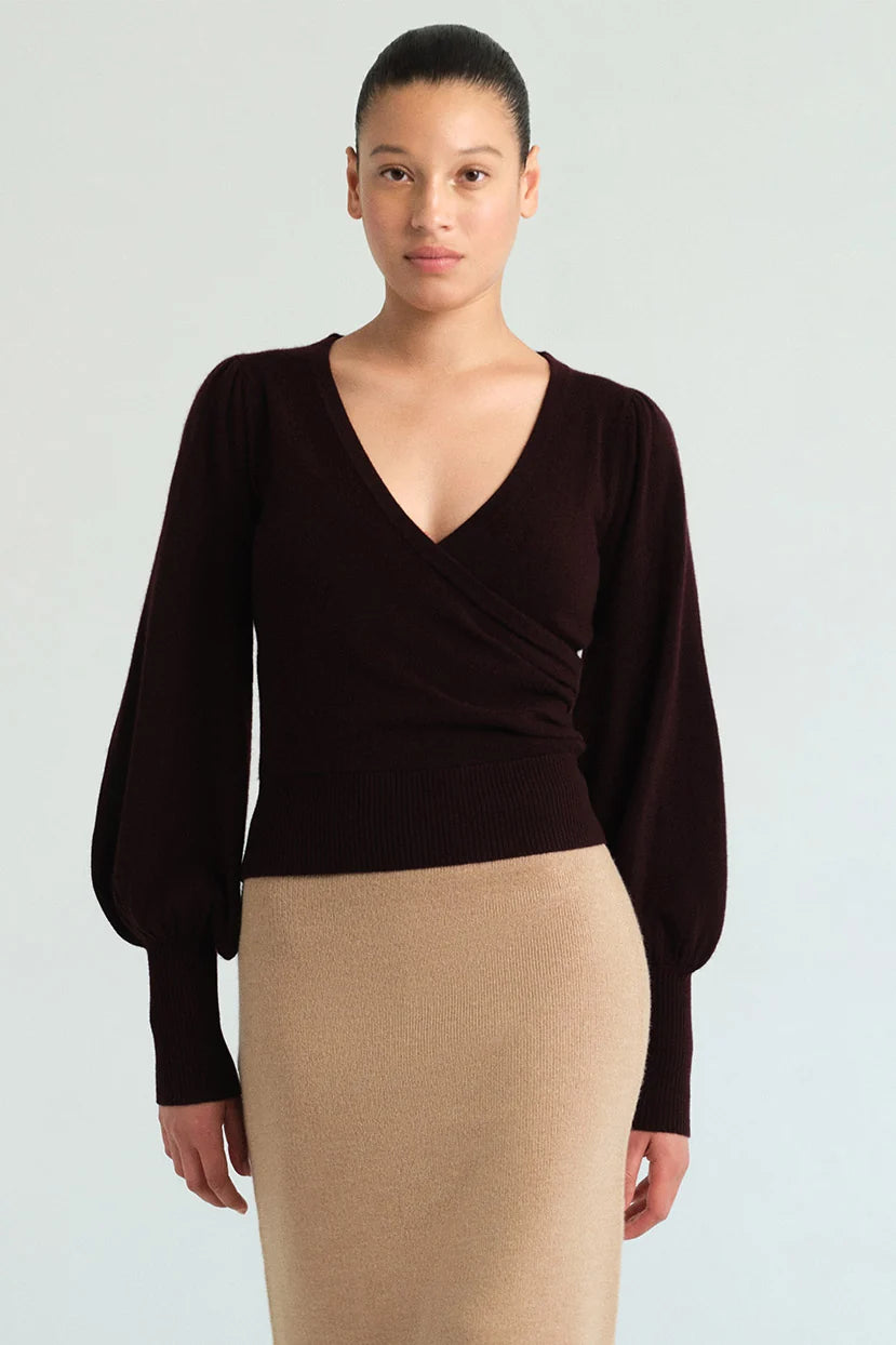 A model wearing a dark brown long-sleeve wrap top with balloon sleeves and a beige knit pencil skirt, photographed against a light gray studio background.