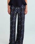 A model is shown from the waist down wearing wide-leg trousers with an intricate blue, black, and white baroque-style pattern, paired with a dark navy peplum top and dark brown pointed shoes.