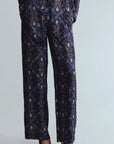 A person wearing dark navy patterned trousers with an ornate medallion print in blue, gold, and white, paired with dark brown pointed-toe heels against a light gray studio background.