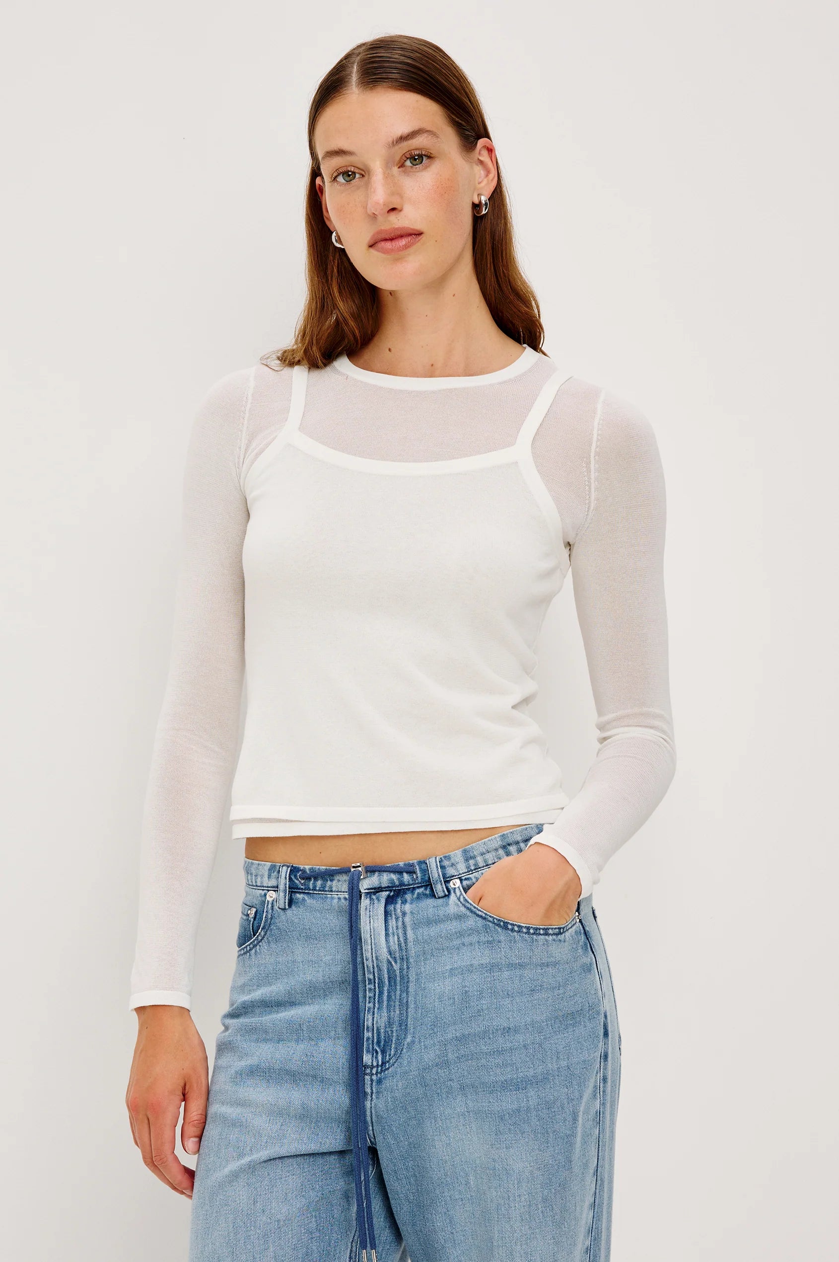 Person wearing a white long-sleeve top and blue jeans on a plain background front view