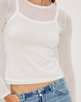 Person wearing a white long-sleeve top and blue jeans on a plain background detail view