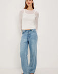 Woman wearing a white tank top and light blue jeans on a plain background front view