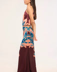 A woman modeling a sleeveless two-piece set with a halter crop top and matching high-waisted skirt, featuring a multicolor abstract print in teal, peach, and deep burgundy on a plain light background.
