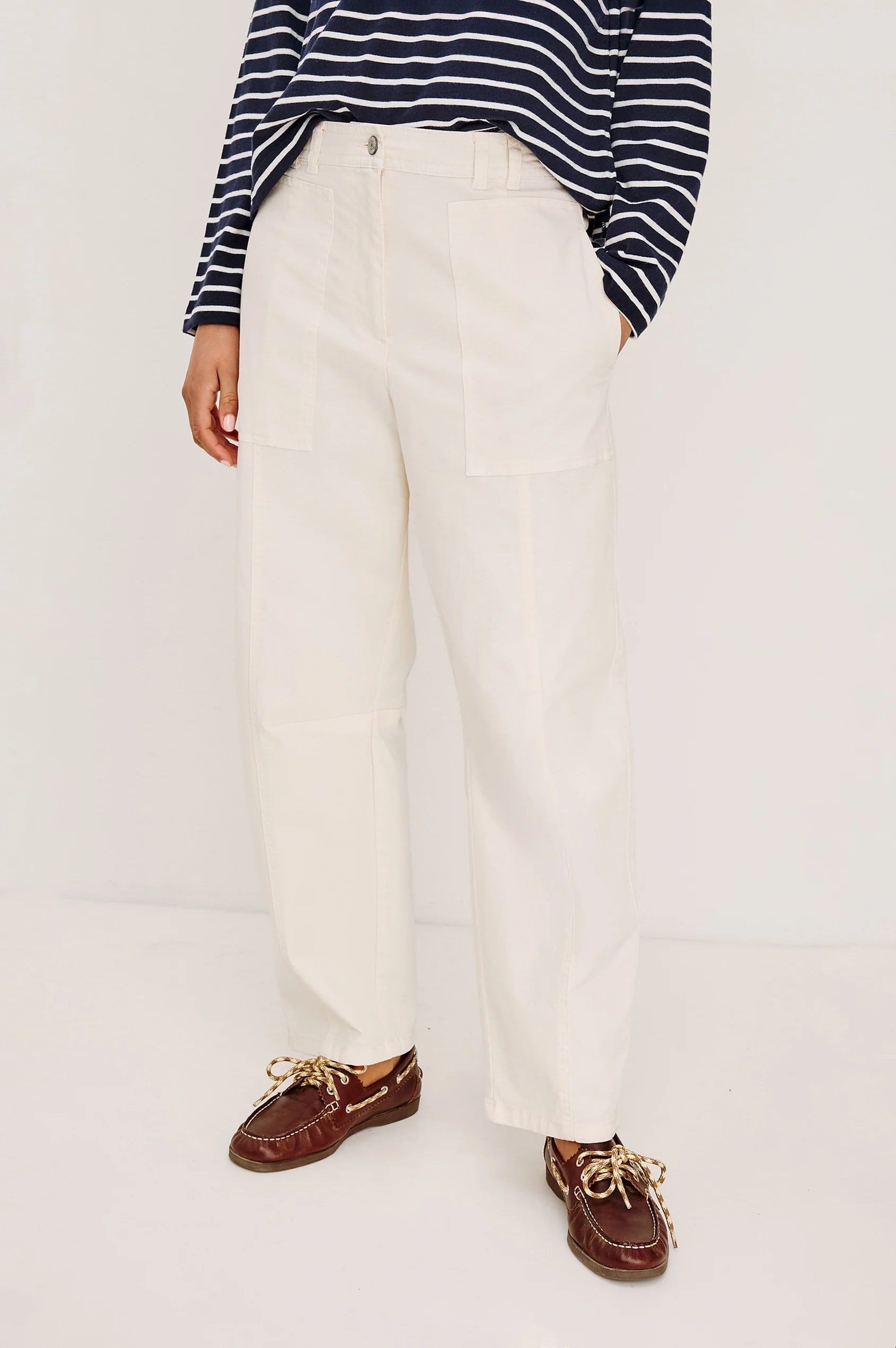 Person wearing a striped shirt, white pants, and brown shoes on a plain background