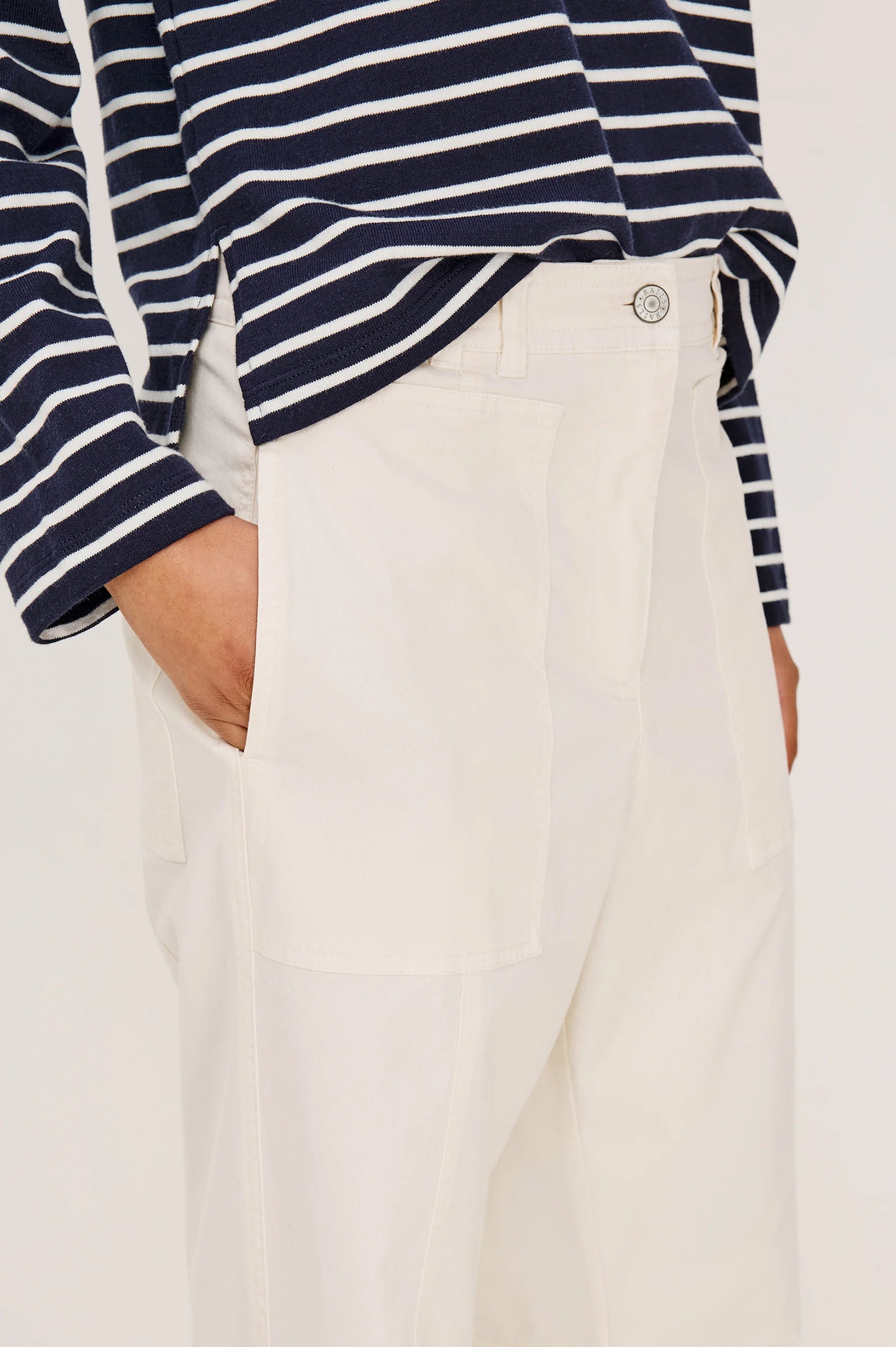Person wearing a navy and white striped shirt with beige pants on a white background