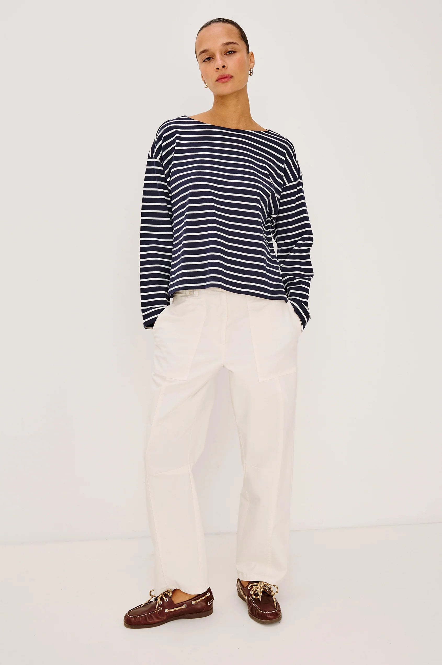 Person wearing a striped sweater, white pants, and brown loafers on a white background