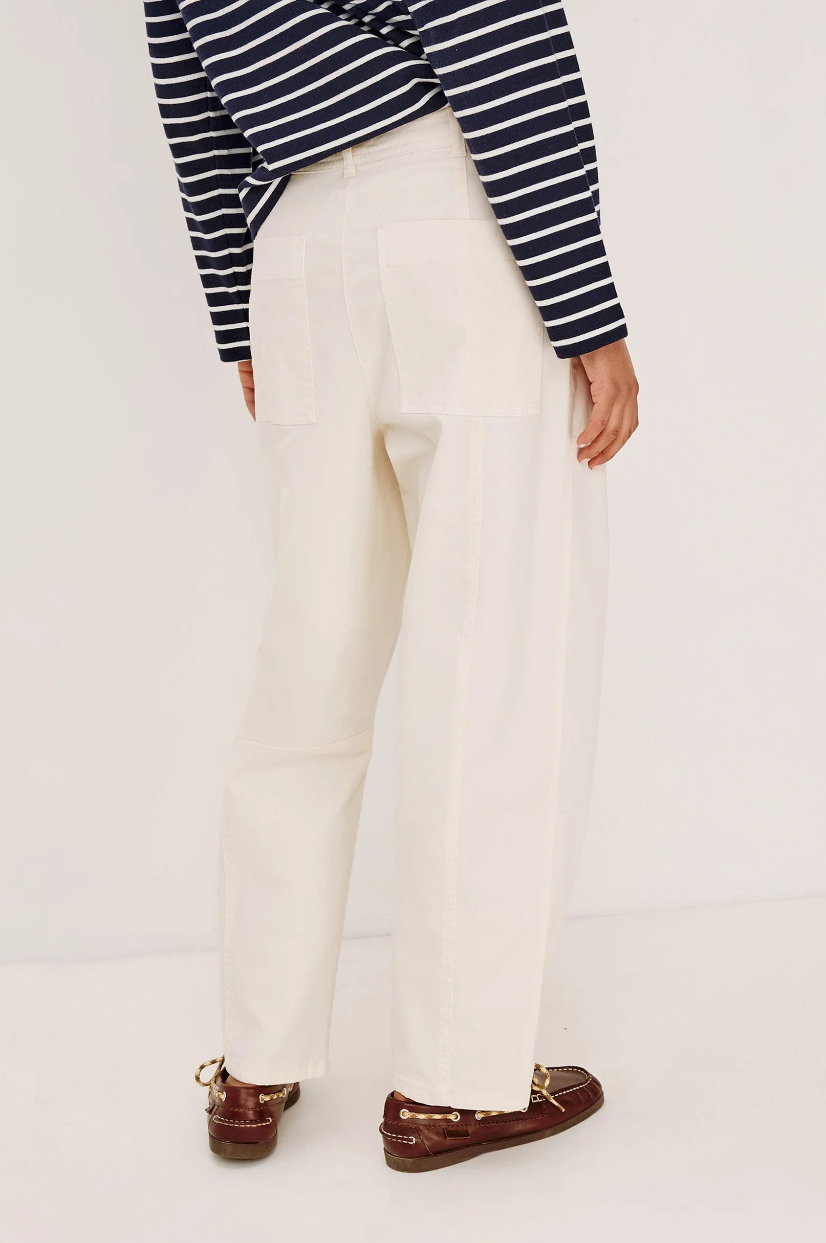 Person wearing a striped shirt, white pants, and brown loafers on a plain background