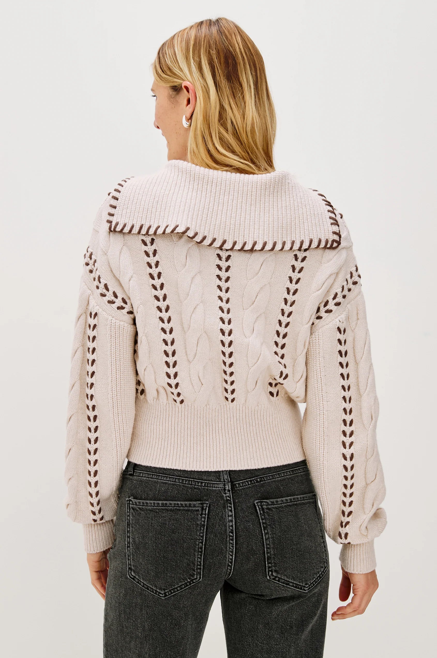 Person wearing a cream-colored sweater with intricate back design on a white background
