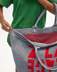 Person holding a striped tote bag with red text against a plain background