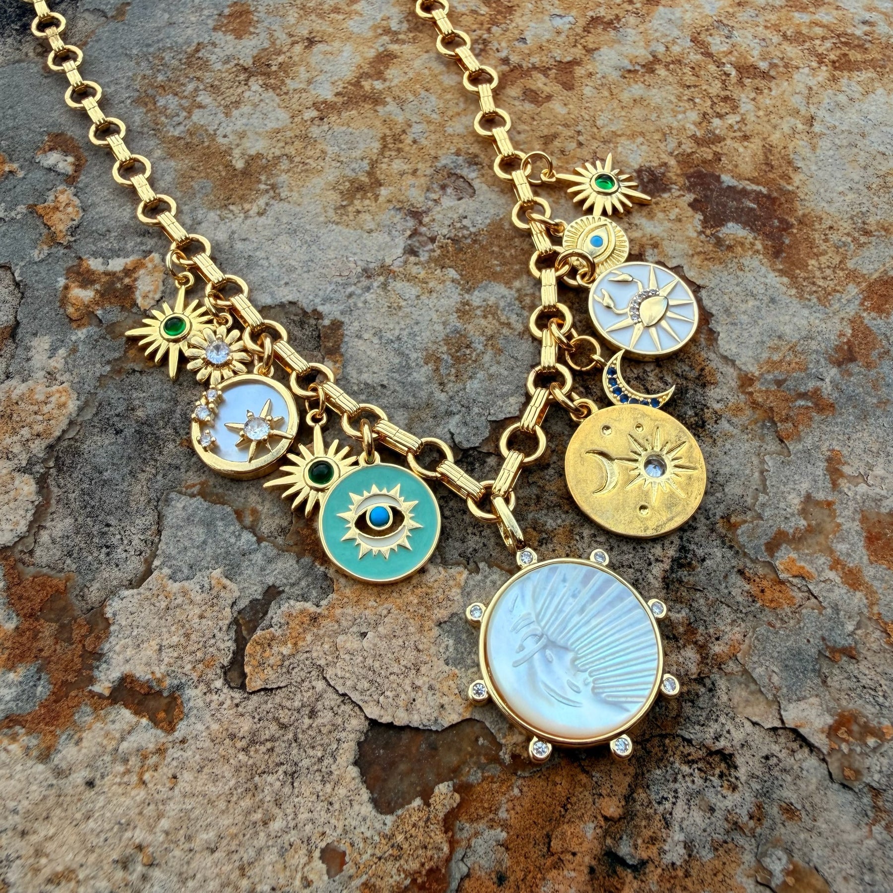 Gold necklace with various charms on a textured stone surface