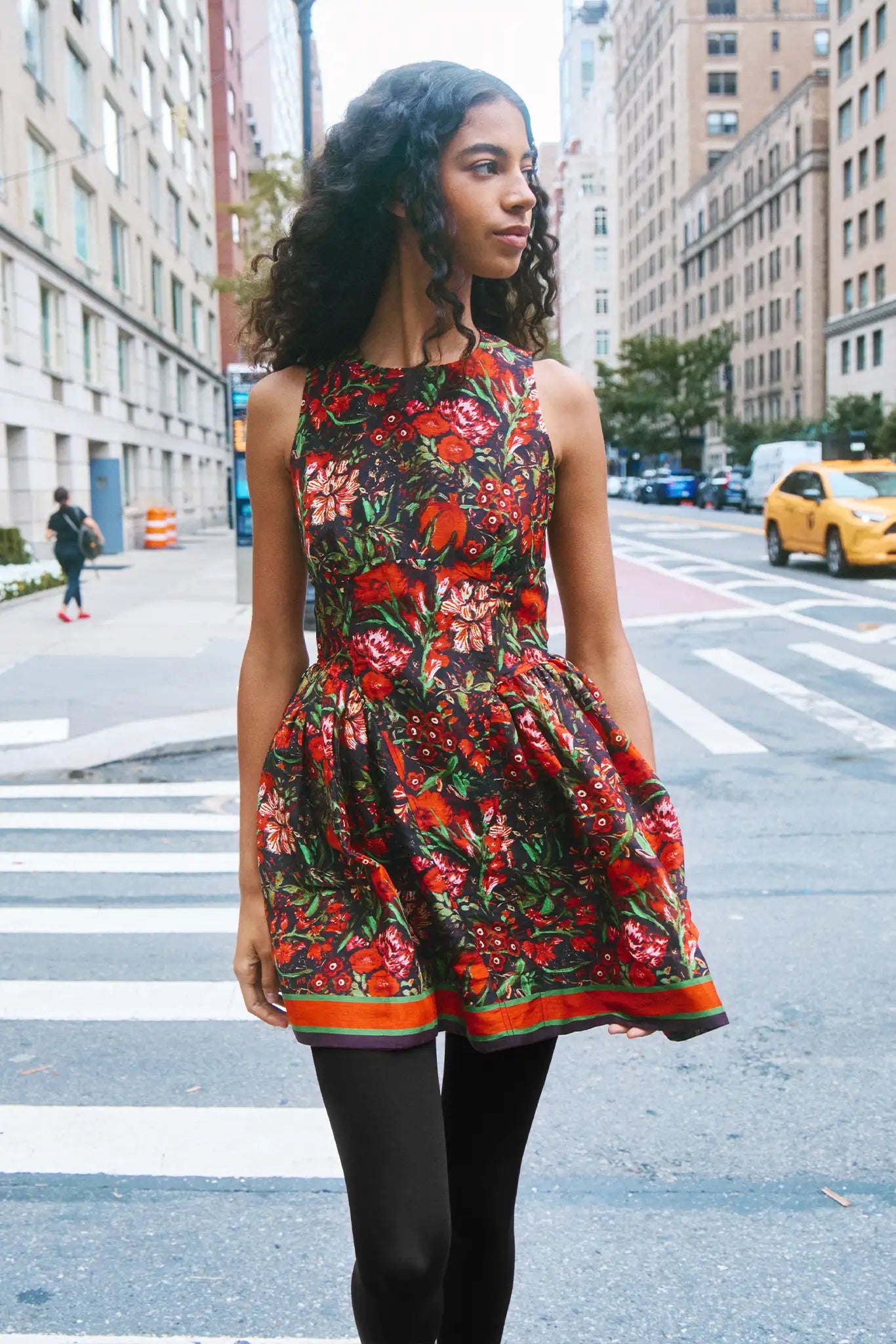 Woman in a colorful floral dress standing on a city street.