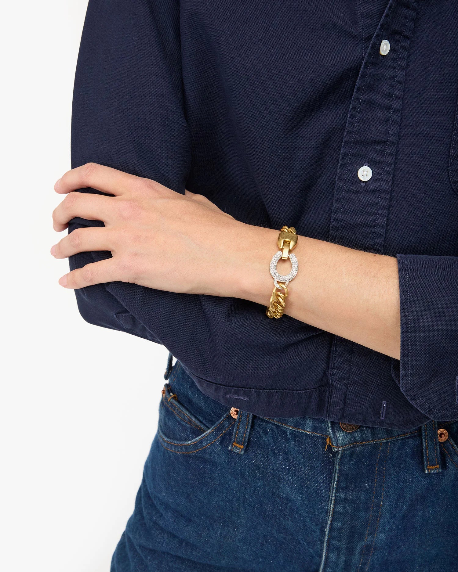 Person wearing a gold and white bracelet on a navy shirt and blue jeans background