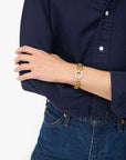 Person wearing a gold and white bracelet on a navy shirt and blue jeans background