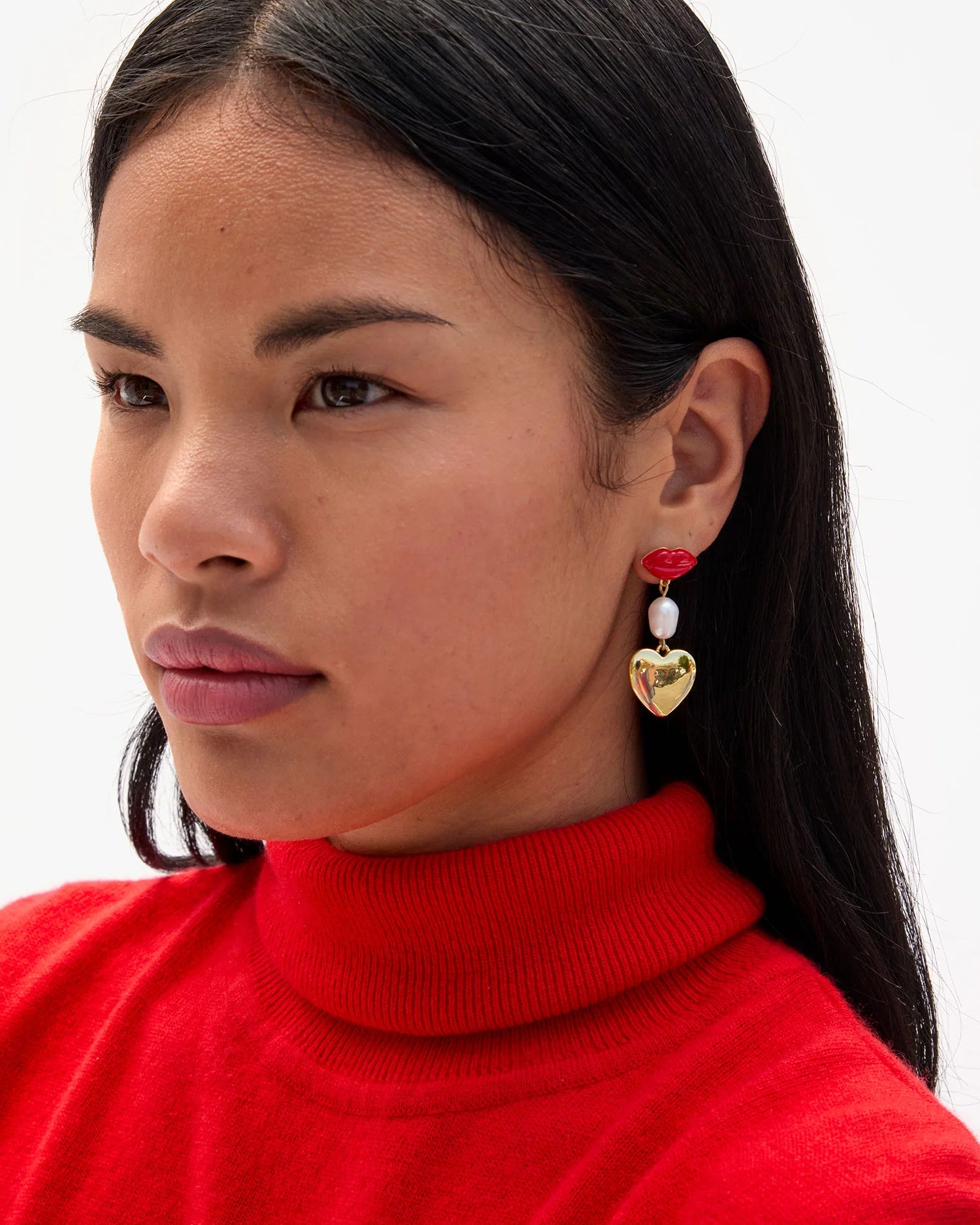 Woman wearing a red turtleneck sweater with heart-shaped earrings on a white background