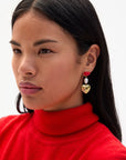 Woman wearing a red turtleneck sweater with heart-shaped earrings on a white background