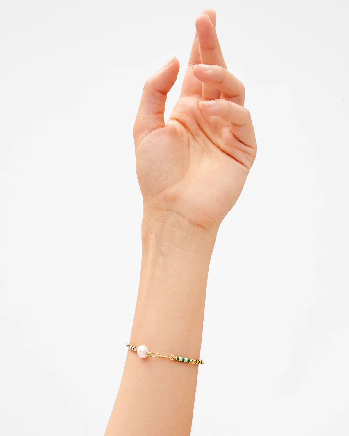 Hand wearing a gold bracelet with a pearl on a light gray background