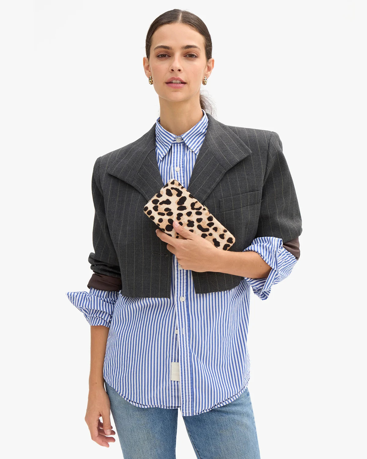 model holding a leopard clutch while wearing a stripe blazer over a stripe shirt on a white background