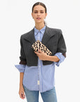 model holding a leopard clutch while wearing a stripe blazer over a stripe shirt on a white background