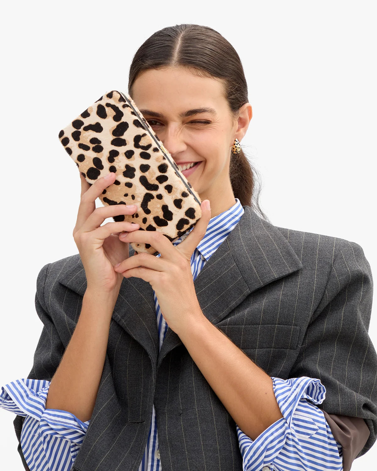 model holding a leopard clutch while wearing a stripe blazer over a stripe shirt on a white background