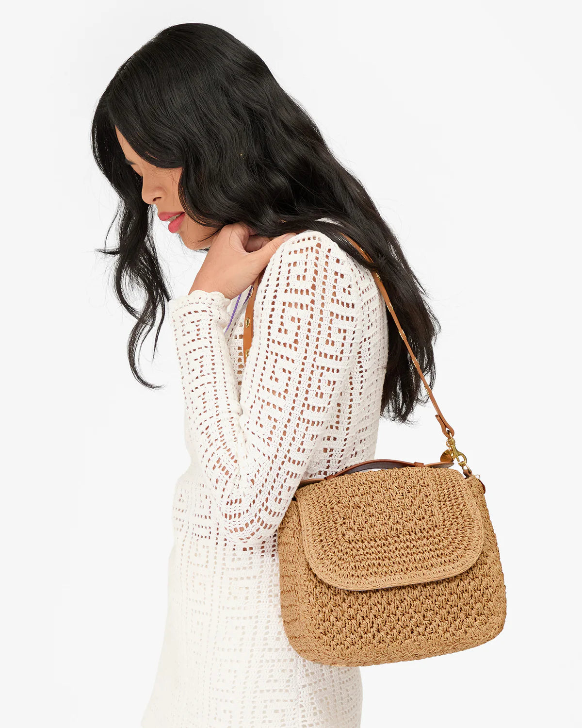 Woman wearing a white crochet top with a brown woven handbag on a white background