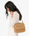 Woman wearing a white crochet top with a brown woven handbag on a white background