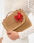 Brown woven handbag with a red lobster charm held by a person wearing a white lace top.