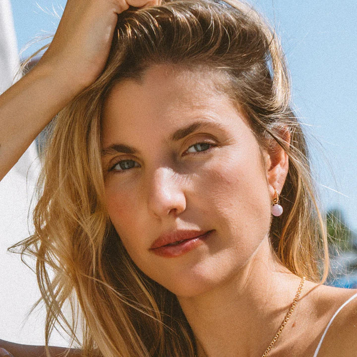 Woman with blonde hair and pink earrings against a blue sky