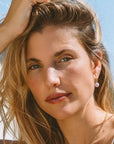 Woman with blonde hair and pink earrings against a blue sky