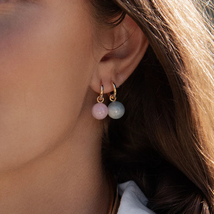 Close-up of a person wearing gold hoop earrings with pink and green beads.
