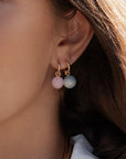 Close-up of a person wearing gold hoop earrings with pink and green beads.