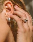 Close-up of a person wearing diamond earrings and a ring, with a blurred background.