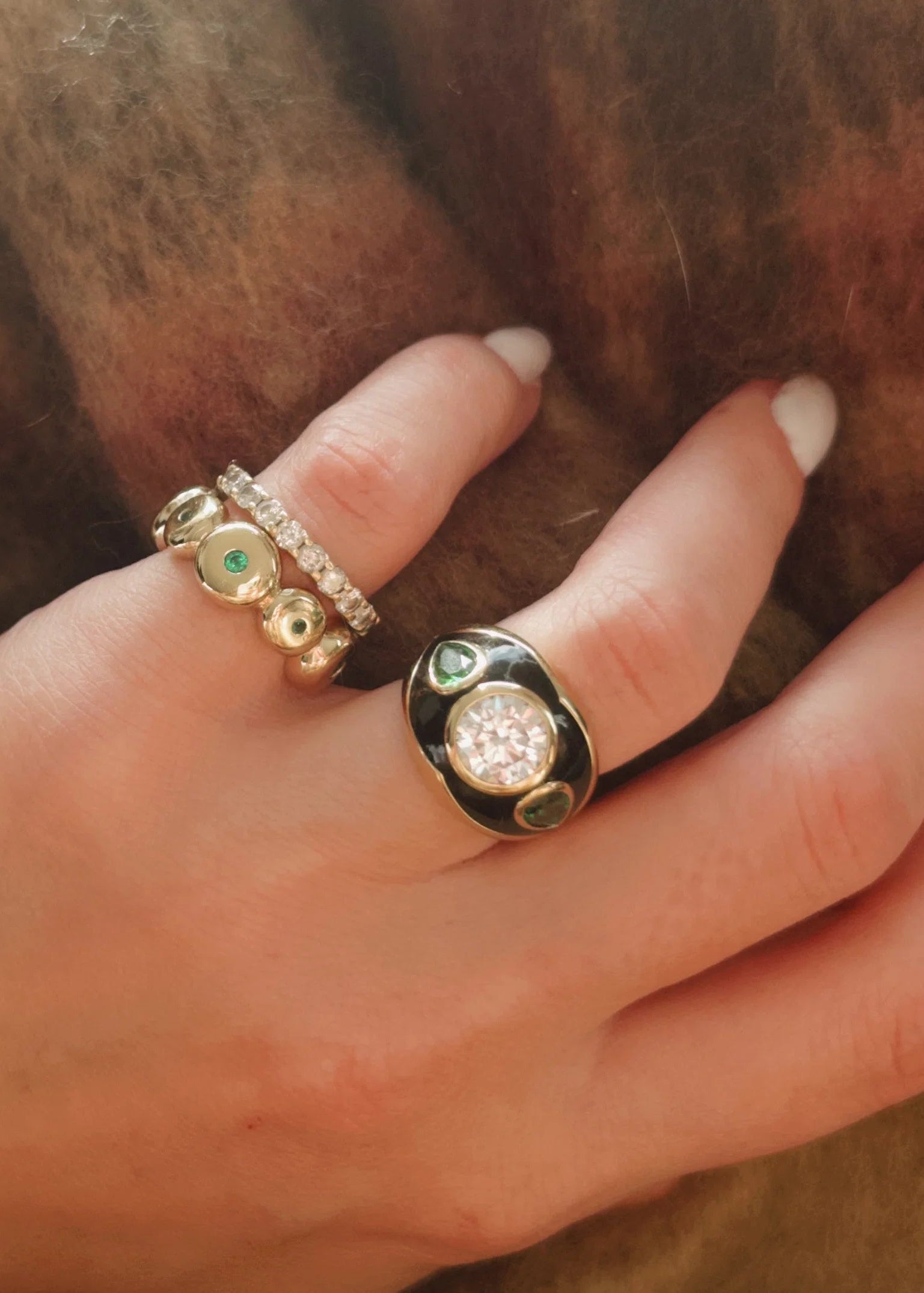 Hand wearing two gold rings with gemstones against a brown background
