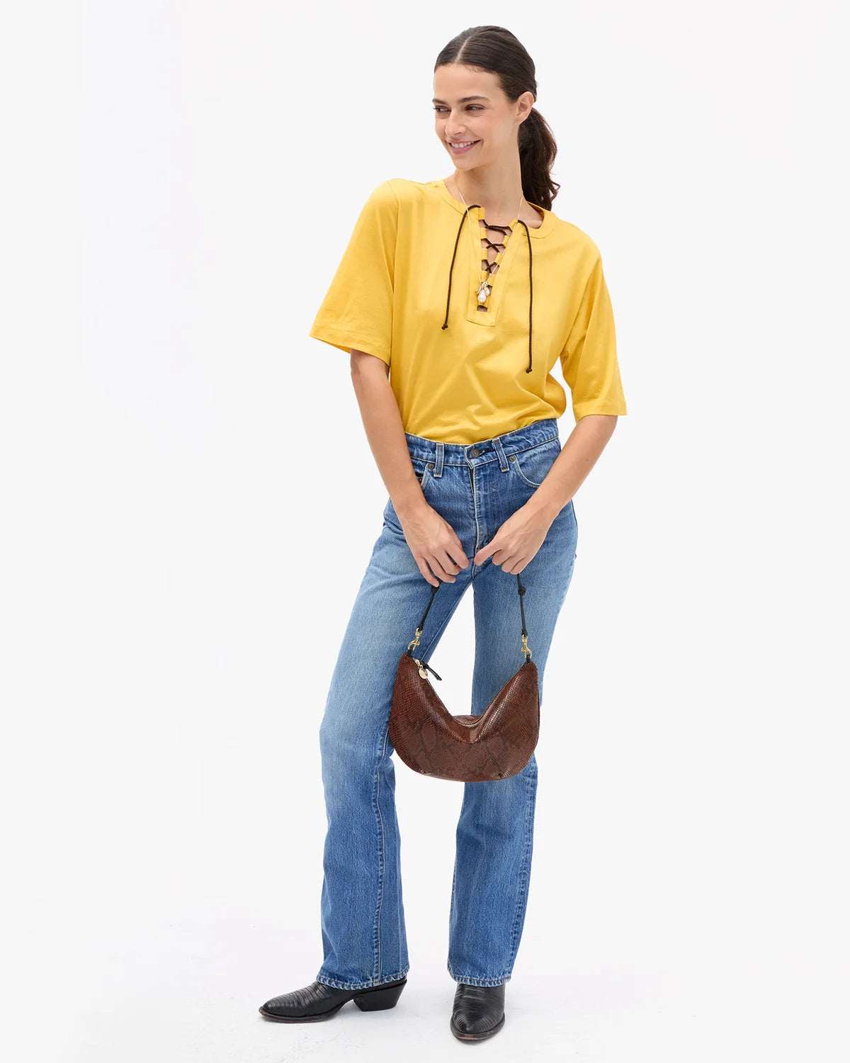 a model in a yellow shirt and jeans wearing the python lune bag on a white background
