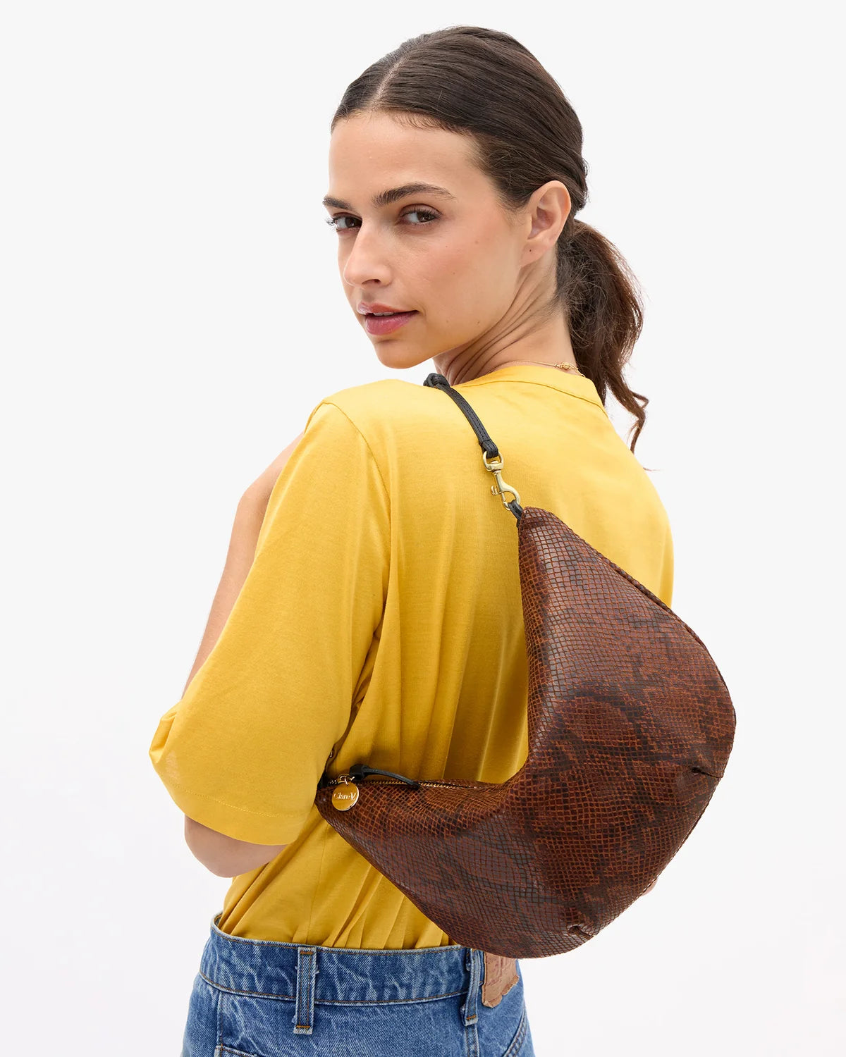 a model in a yellow shirt wearing the python lune bag on a white background