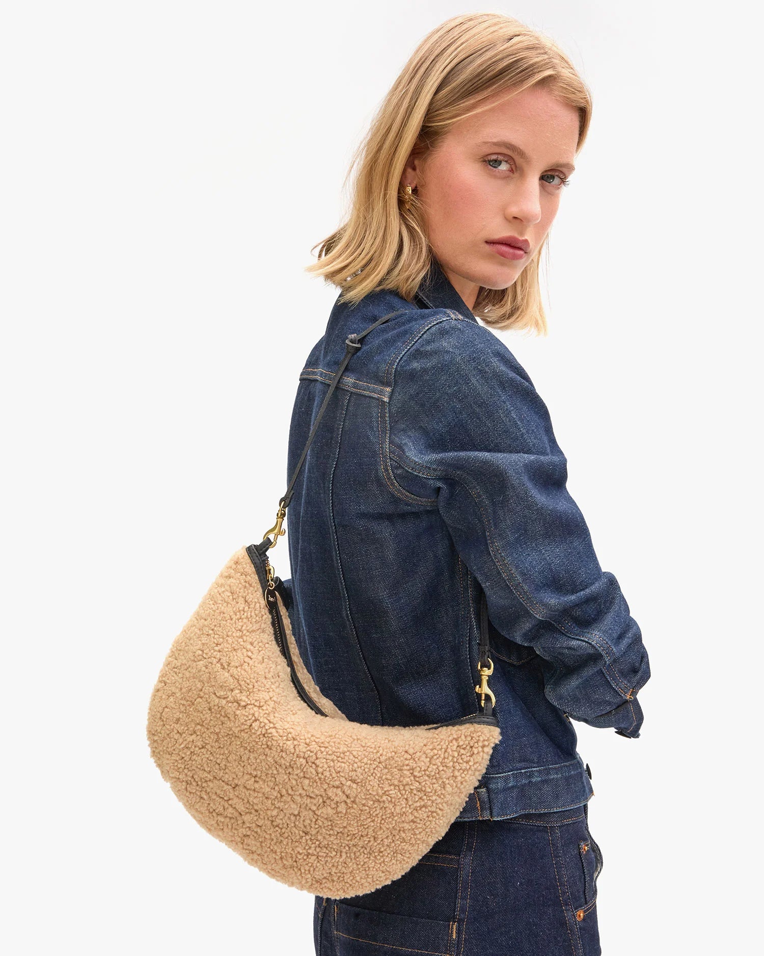 Woman wearing a denim jacket with a beige and brown handbag on a white background