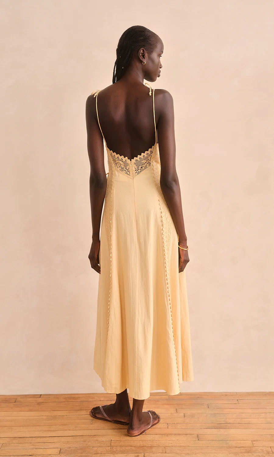 Woman wearing a yellow dress with lace detailing on a beige background, back