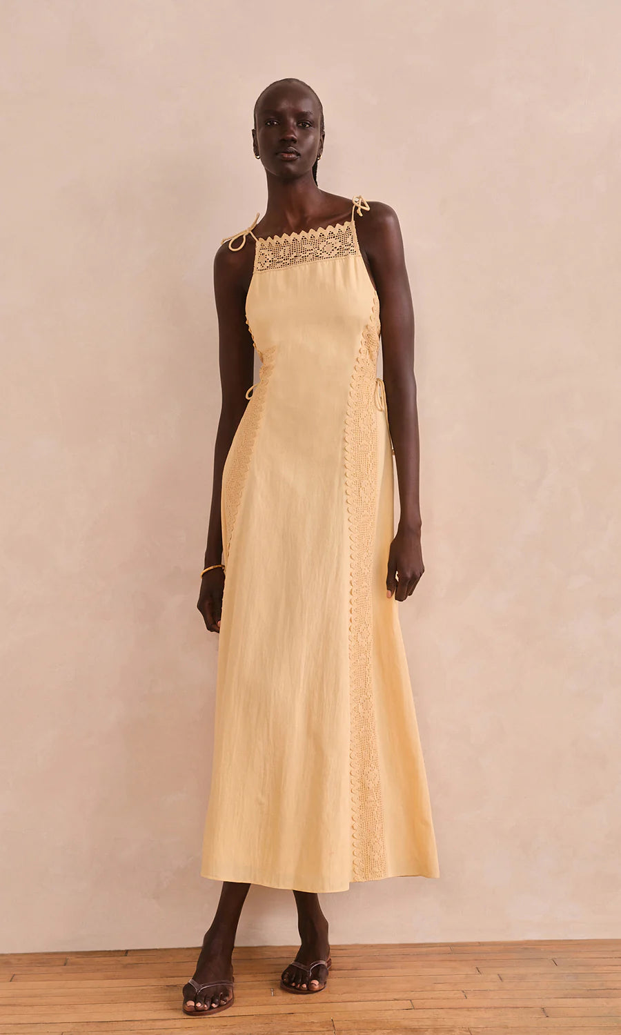 Woman wearing a pale yellow dress with lace details against a plain background, front