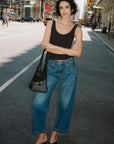 Woman standing on a city street wearing a black tank top and blue jeans.