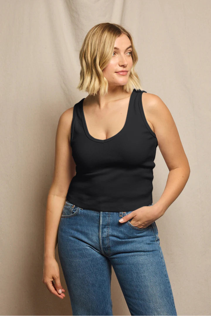 Woman wearing a black tank top and blue jeans against a beige background, size L