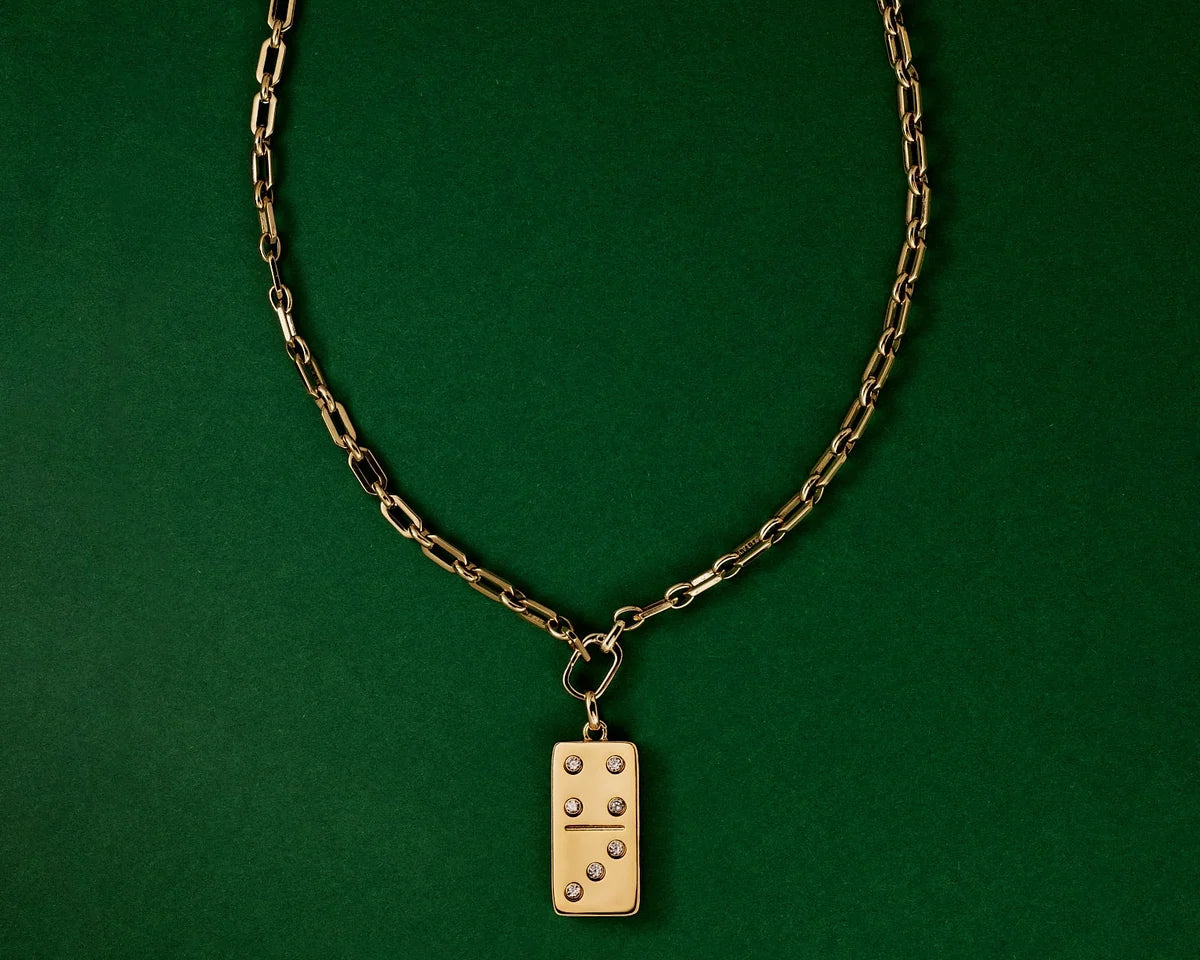 A gold-tone chain necklace with a rectangular domino pendant, displayed against a solid dark green background.