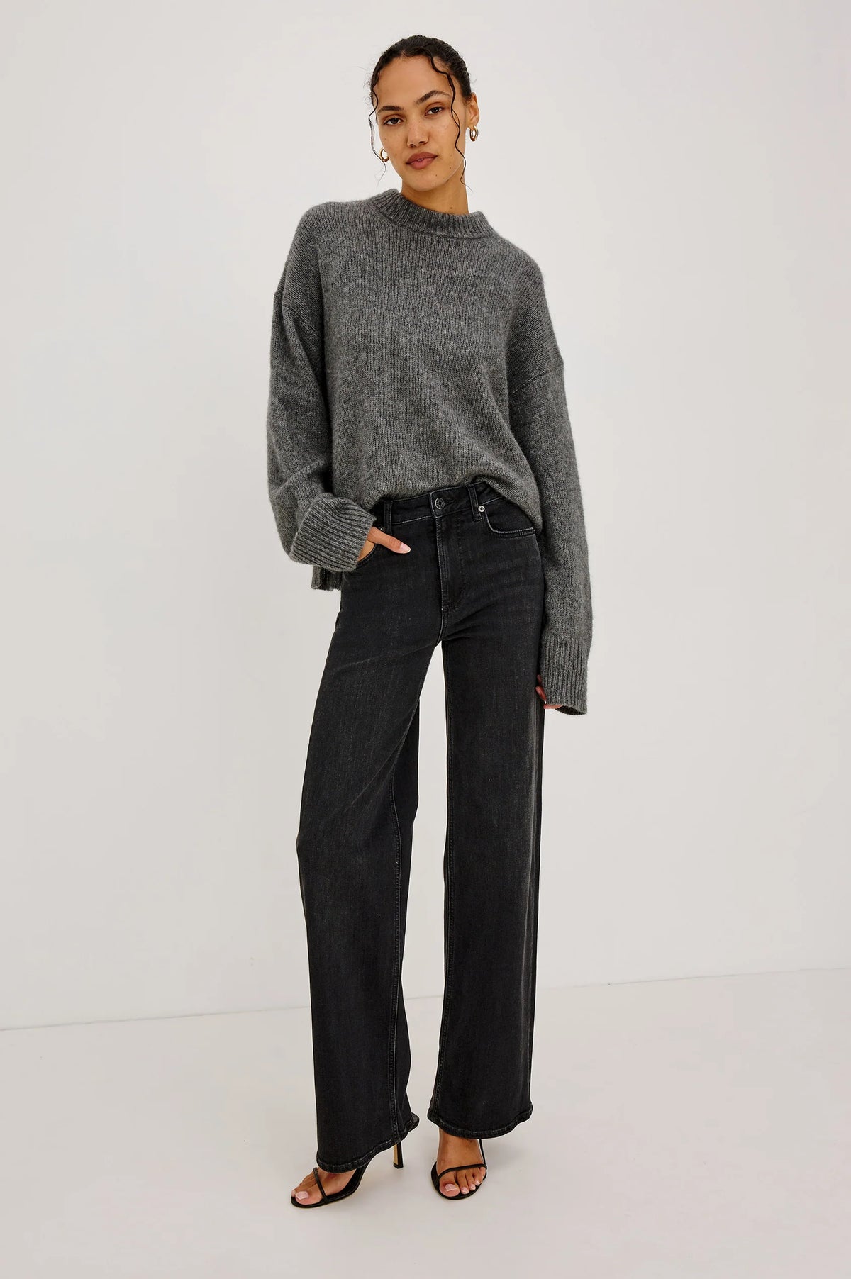 model wearing a grey sweater with black jeans on a grey background