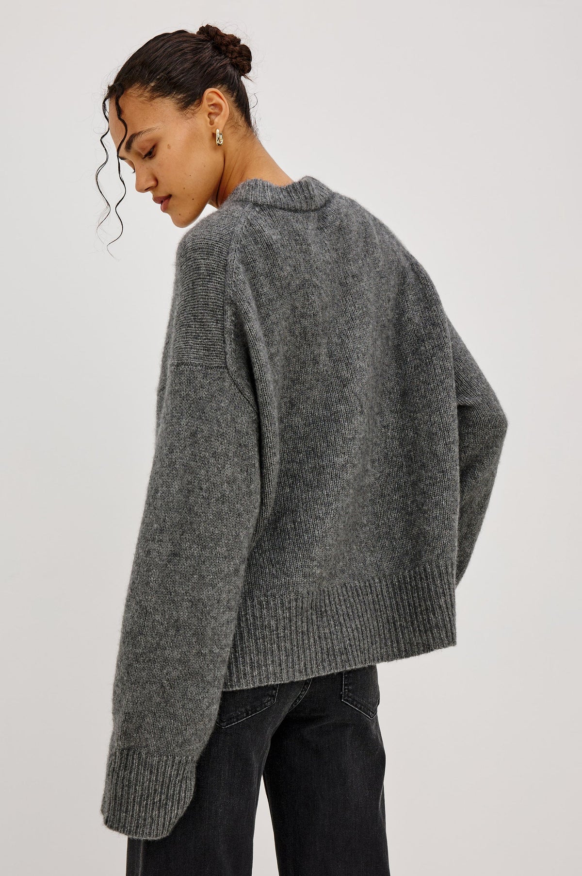 model wearing a grey sweater with black jeans on a grey background, back view