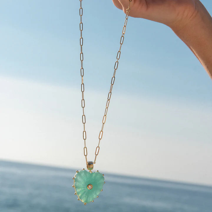 Necklace with a heart-shaped green pendant held against a blue sky and ocean background