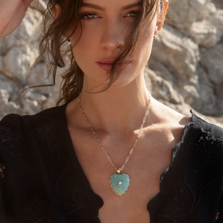 Woman wearing a necklace with a heart-shaped pendant against a stone wall background